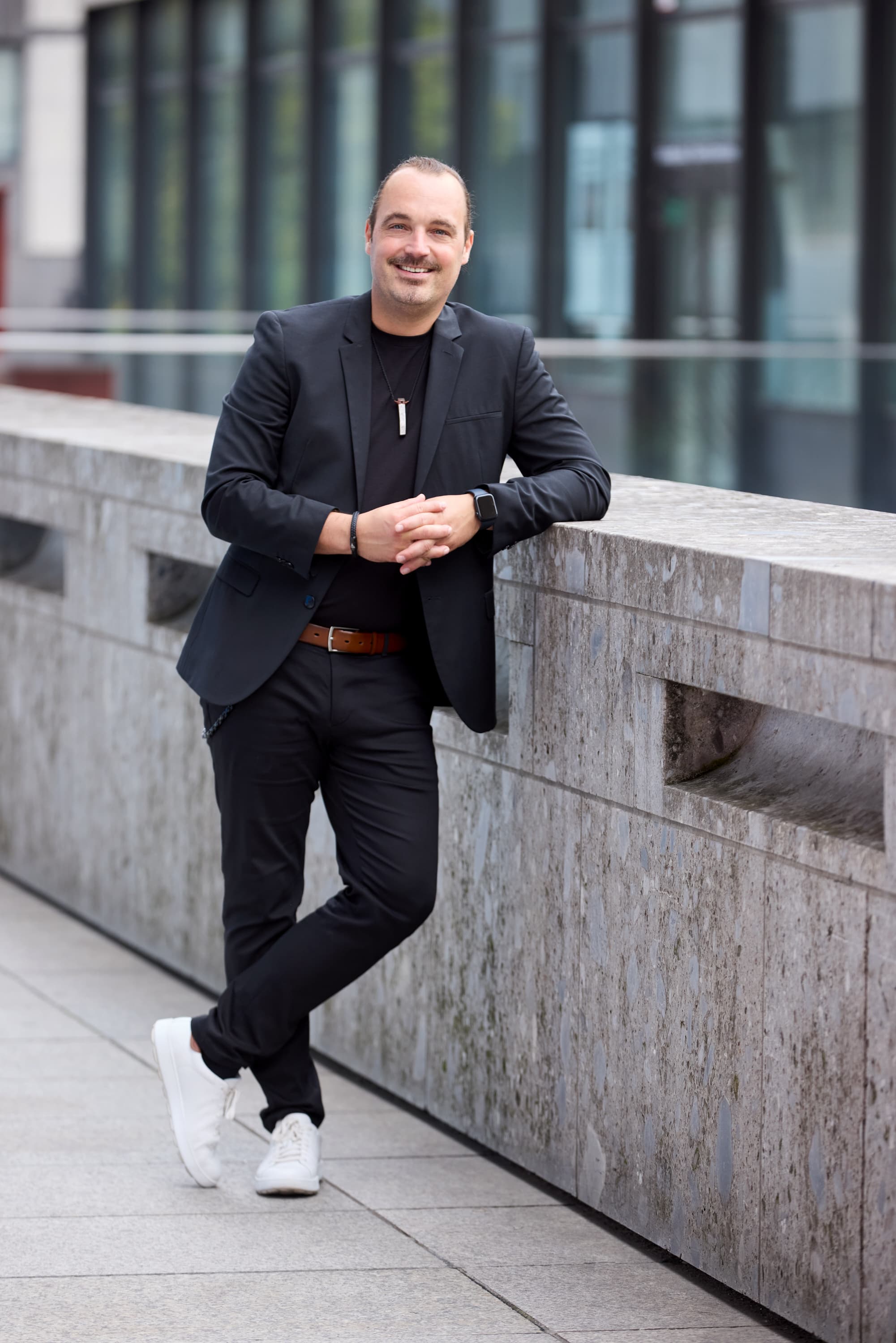 Markus Wessel in Blazer und weißen Sneakern, an einer Steinwand gelehnt